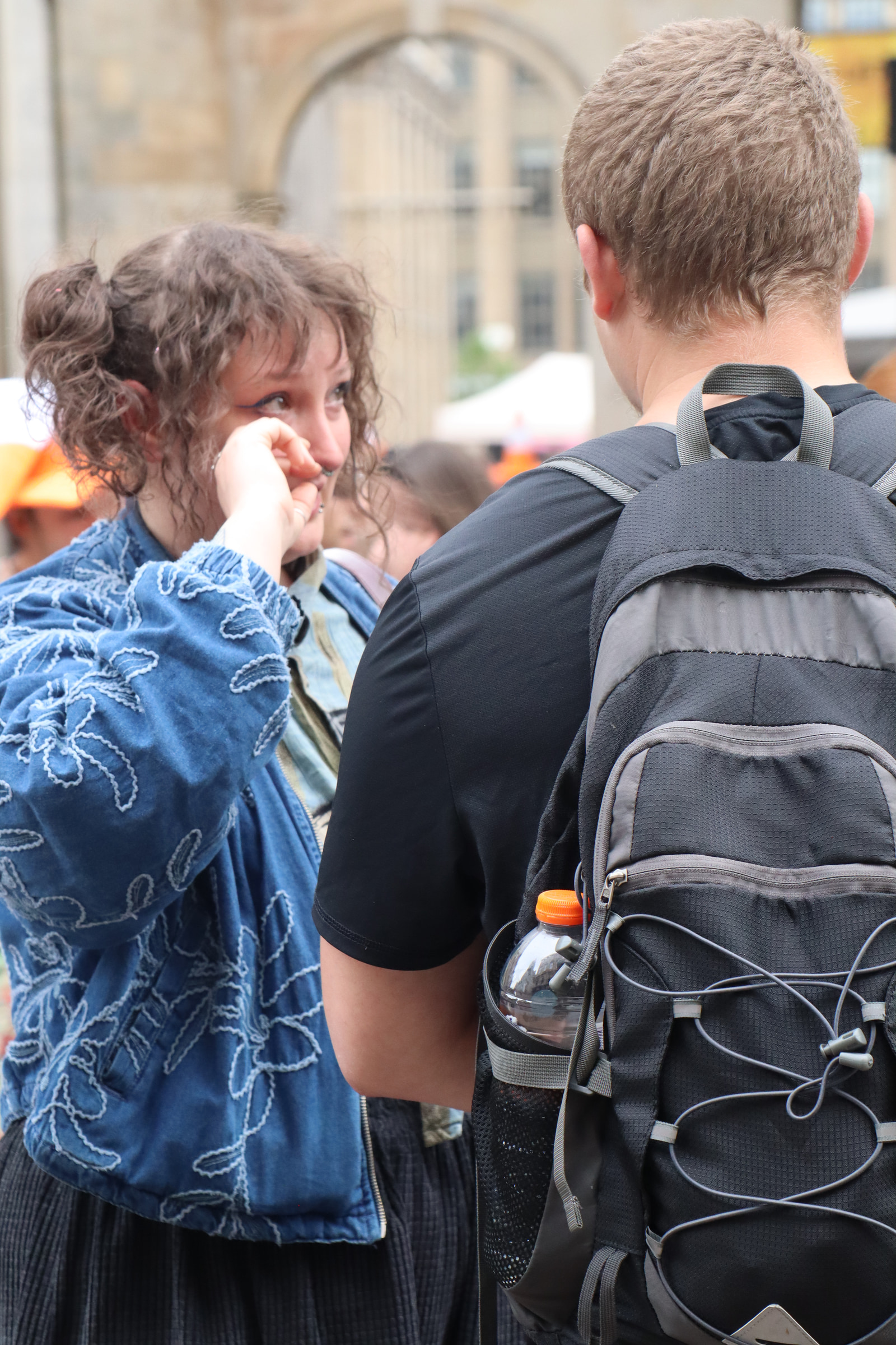 A man and a woman stand close together, facing each other, in an outdoor public space.